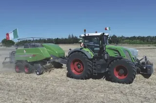 Zelený traktor Fendt táhne lis na balíky po suchém strništi.