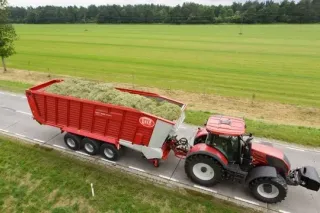 Červený traktor táhne naložený sběrací vůz Lely po silnici