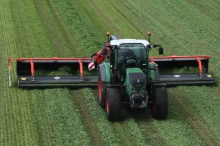 Traktor s širokým shrnovačem Kuhn na louce