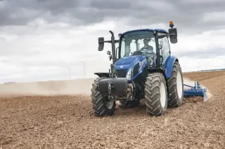 Modrý traktor New Holland při práci na poli