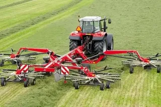 Traktor se širokým shrnovačem píce na louce