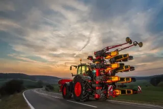 Traktor převáží složený žací stroj na silnici při západu slunce