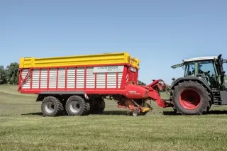 Červenožlutý sběrací vůz Pöttinger Torro tažený traktorem na louce.