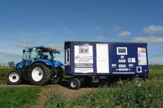 Modrý traktor New Holland táhne obytný přívěs po cestě
