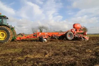 Oranžový hloubkový kypřič Kuhn Performer 3000 tažený traktorem při práci na poli.