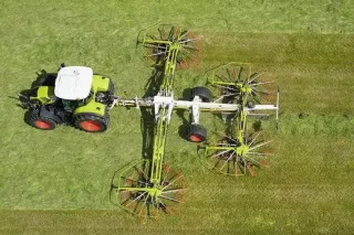 Traktor Claas s rozloženým shrnovačem píce na louce