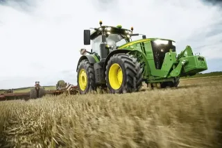 Zelený traktor John Deere při práci na poli