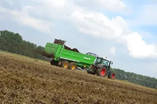 Zelený traktor táhne rozmetadlo hnoje Joskin po poli