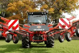 Červený shrnovač Kuhn za traktorem na trávníku