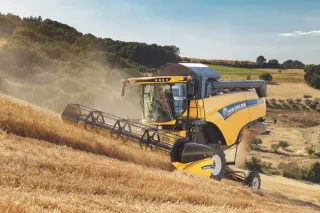 Žlutá sklízecí mlátička New Holland sklízí obilí ve svahu