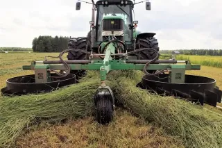 Traktor se zeleným shrnovačem Agronic na louce.