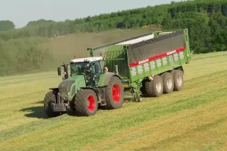 Traktor Fendt táhne zelený senážní vůz Bergmann Shuttle po poli