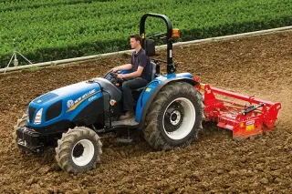 Modrý traktor New Holland s rotavátorem na poli