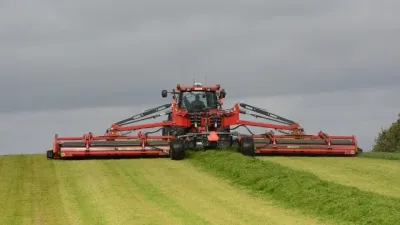 Červený traktor s širokou žací kombinací na louce