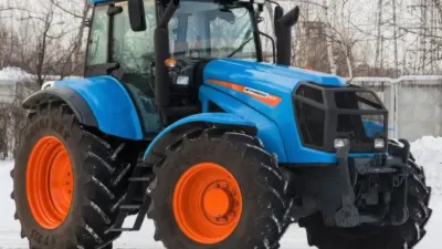 Modrý traktor Agromash se zářivě oranžovými koly na sněhu