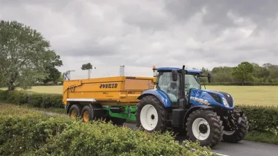 Modrý traktor New Holland se žlutým návěsem na silnici