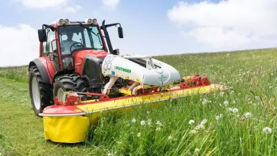 Červený traktor s čelní žací lištou Pöttinger na louce