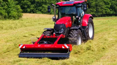Červený traktor Case IH se žacím strojem na louce