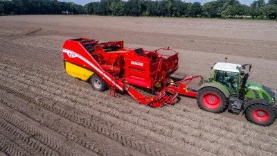 Červený sklízeč Grimme Evo 280 tažený traktorem na poli