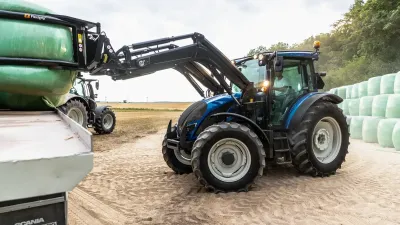 Modrý traktor Valtra nakládá balíky na vůz