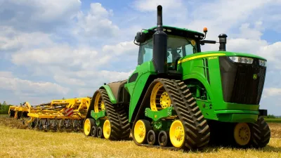 Zelený pásový traktor John Deere s kypřičem na poli