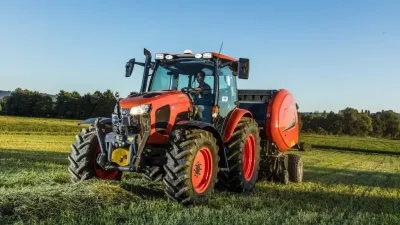 Oranžový traktor Kubota s lisem na louce