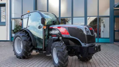 Tmavý traktor Carraro před budovou