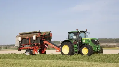 Traktor John Deere s pásovým shrnovačem Kuhn na louce