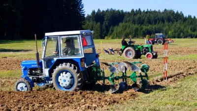Modrý traktor s pluhem při soutěži v orbě