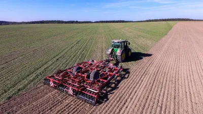 Traktor s červeným kultivátorem Kverneland při práci na poli