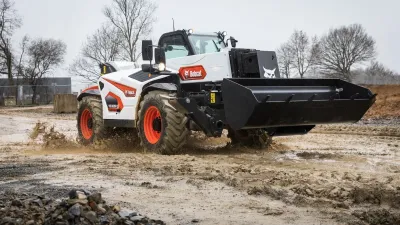 Bílý teleskopický manipulátor Bobcat na staveništi