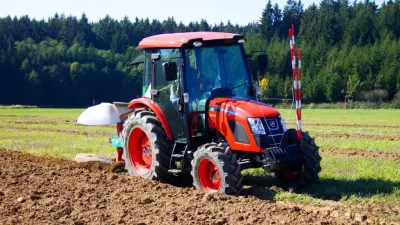 Oranžový traktor s pluhem při orbě
