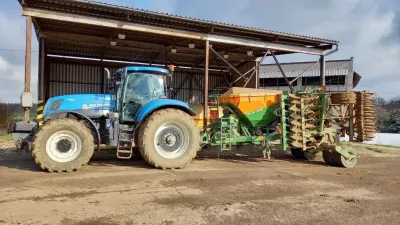Modrý traktor New Holland s připojeným secím strojem Amazone před přístřeškem