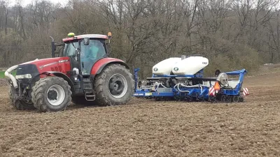 Červený traktor Case IH se secím strojem Kinze 3500 při setí na poli