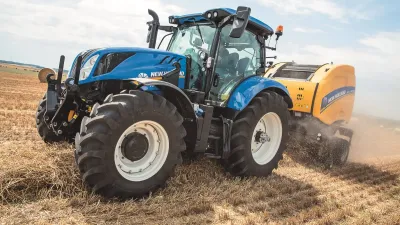 Modrý traktor New Holland s lisem na slámu při práci na poli