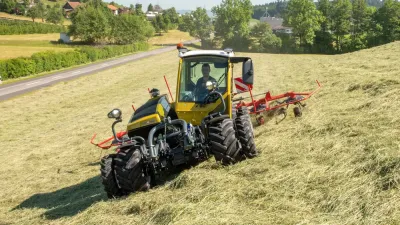 Žlutý traktor Rigitrac s obracečem píce na horské louce