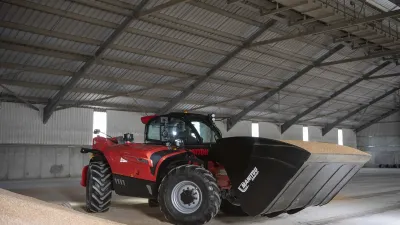 Červený teleskopický manipulátor Manitou s velkou lopatou ve skladu