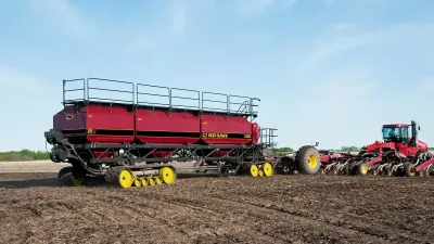 Velký červený secí stroj Seed Hawk tažený traktorem na poli