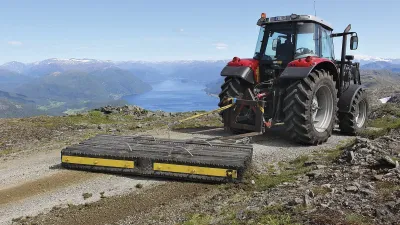 Traktor s taženým grejdrem na horské cestě