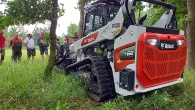 Pásový nakladač Bobcat při předvádění mezi stromy.
