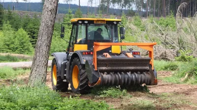 Žlutočerný traktor s oranžovým lesním mulčovačem pracuje na lesní cestě.