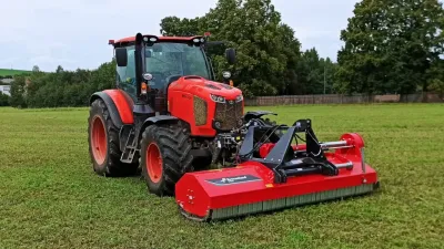 Červený traktor Kubota M6002 s mulčovačem na travnaté ploše.