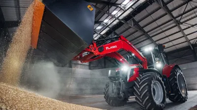 Červený traktor Massey Ferguson s čelním nakladačem přesypává obilí v hale.