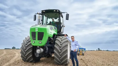 Zelený hybridní traktor AUGA stojí na poli vedle muže.