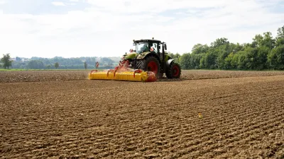 Traktor táhne žluté rotační brány Pöttinger po zpracovaném poli.