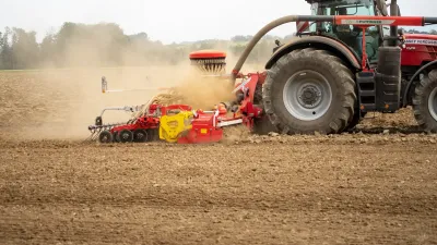 Traktor Massey Ferguson táhne pneumatický secí stroj Pöttinger na poli.