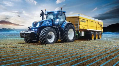Modrý traktor New Holland T7 HD táhne žlutý přívěs na poli.
