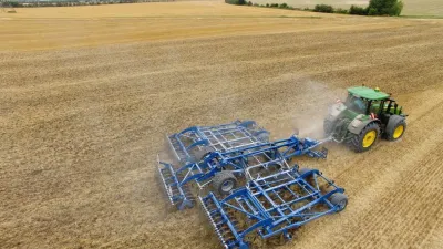 Traktor táhne široký modrý kypřič Köckerling Allrounder Flatline po poli.