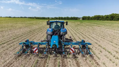 Modrý traktor New Holland s meziřádkovým kypřičem na poli.