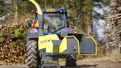 Žlutočerný štěpkovač Junkkari HJ252 G připojený k traktoru před hromadou dřeva.